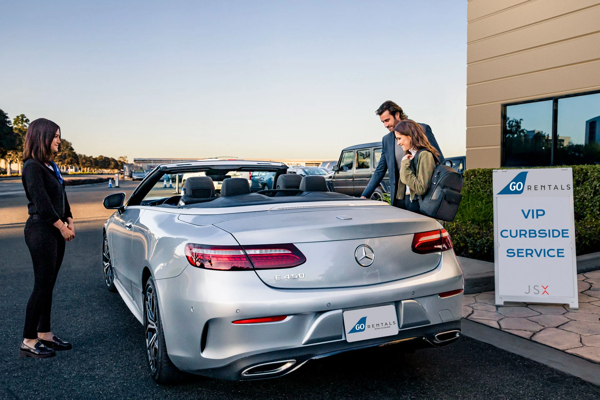 A man and woman getting into a luxury car with an airport personnel nearby.