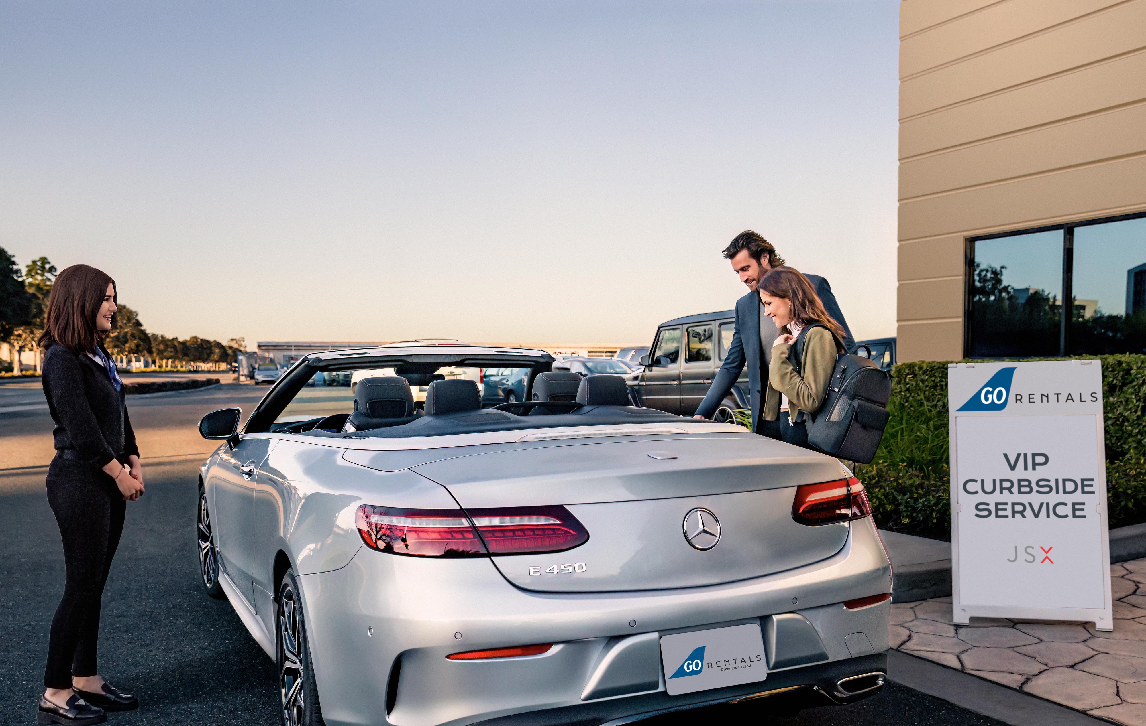 A man and woman getting into a luxury car with an airport personnel nearby.